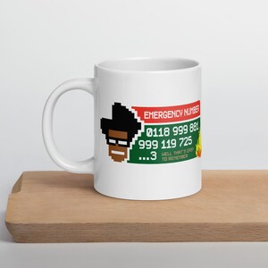 May include: White ceramic mug featuring a pixelated image of a man with glasses and the text "EMERGENCY NUMBER" and phone numbers. The mug also includes the phrase "HELL THAT'S EASY TO REMEMBER".