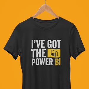 Pode incluir: Camiseta preta com texto branco que diz "I've got the Power BI" com um logotipo amarelo do Power BI.