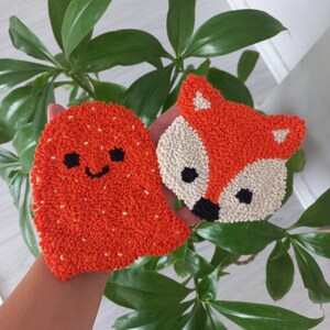 Könnte beinhalten: Zwei orangefarbene und weiße Filz-Streichgarnarbeiten. Eine ist ein Geist mit einem lächelnden Gesicht und die andere ist ein Fuchs mit schwarzen Augen und einer schwarzen Nase.