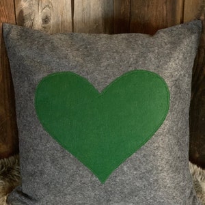Puede incluir: Almohada de fieltro gris con un corazón de fieltro verde en el centro.