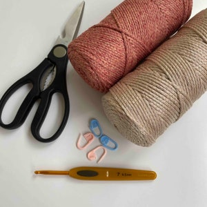 May include: Overhead shot of craft supplies, including two yarn skeins in rose and beige, black scissors, stitch markers, and a crochet hook. The hook is size 7, 4.5mm. Ideal for knitting and crochet projects.