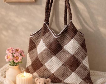 May include: A crochet tote bag featuring a brown and cream diamond checkered pattern. The bag has two long shoulder straps and a white stitched trim along the top edge. The construction consists of a dense, textured yarn stitch throughout.