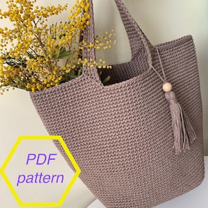 May include: A brown crocheted tote bag with a wooden bead and tassel. The bag is large enough to hold a bouquet of yellow mimosa flowers. The image includes the text "PDF pattern".