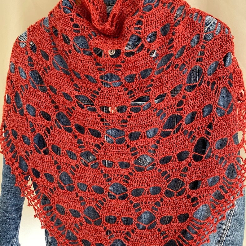 Puede incluir: Un chal de ganchillo rojo con un patr&oacute;n de encaje. El chal est&aacute; drapeado sobre una chaqueta vaquera.