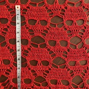 Puede incluir: Primer plano de un encaje de ganchillo rojo con un patr&oacute;n de calavera. El encaje se mide con una regla en pulgadas.