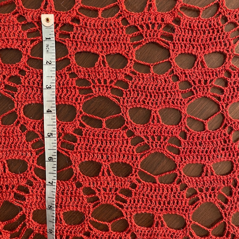 Puede incluir: Primer plano de un encaje de ganchillo rojo con un patr&oacute;n de calavera. El encaje se mide con una regla en pulgadas.