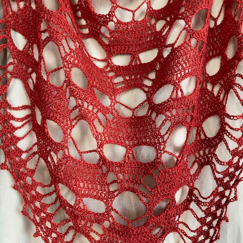 Puede incluir: Un chal de ganchillo rojo con un dise&ntilde;o de calavera. El chal est&aacute; hecho de un patr&oacute;n delicado y calado.