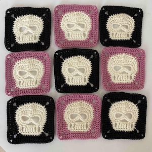 May include: Nine crocheted squares with skull designs. The skulls are off-white, set against black and pink backgrounds. The squares are arranged in a 3x3 grid, showcasing the repeating pattern of the skull motif.