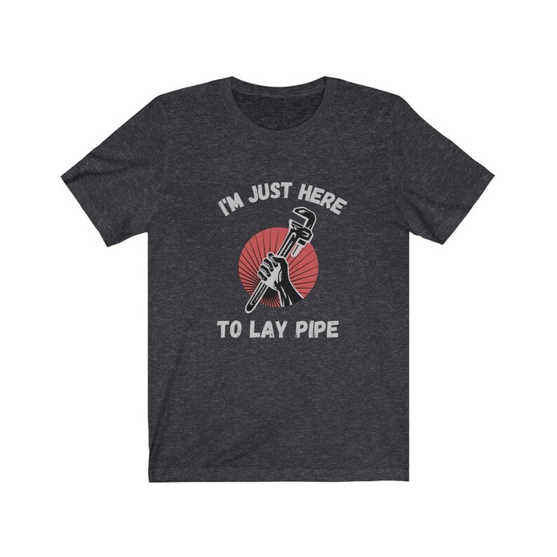 May include: Dark heather grey t-shirt with a red and white graphic of a hand holding a wrench. The text "I'm just here to lay pipe" is printed in white on the shirt.