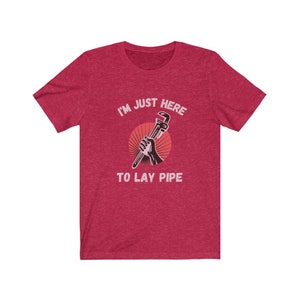 May include: Red heather t-shirt with a graphic of a hand holding a wrench with the text "I'm just here to lay pipe".