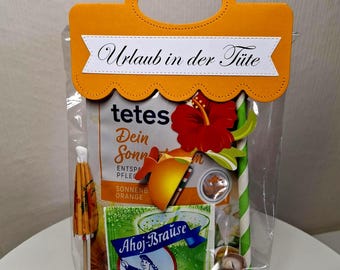 May include: A clear plastic gift bag with an orange paper handle topper labeled "Urlaub in der Tüte." Inside are Ahoj-Brause powder, a small cocktail umbrella, a green and white striped paper straw, seashells, and a packet of orange-scented lotion.