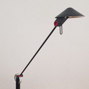 May include: A black desk lamp with a long, adjustable arm and a black shade. The lamp has a red accent on the arm and a black base.