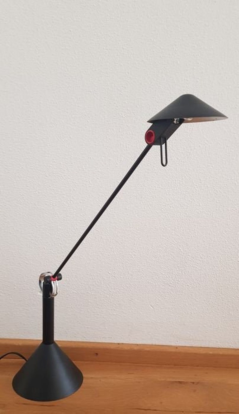 May include: A black desk lamp with a long, adjustable arm and a black shade. The lamp has a red accent on the arm and a black base.