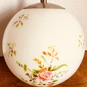 Peut inclure: Un luminaire suspendu en forme de globe en verre blanc avec un motif floral. Les fleurs sont peintes dans des tons de rose, jaune et vert.