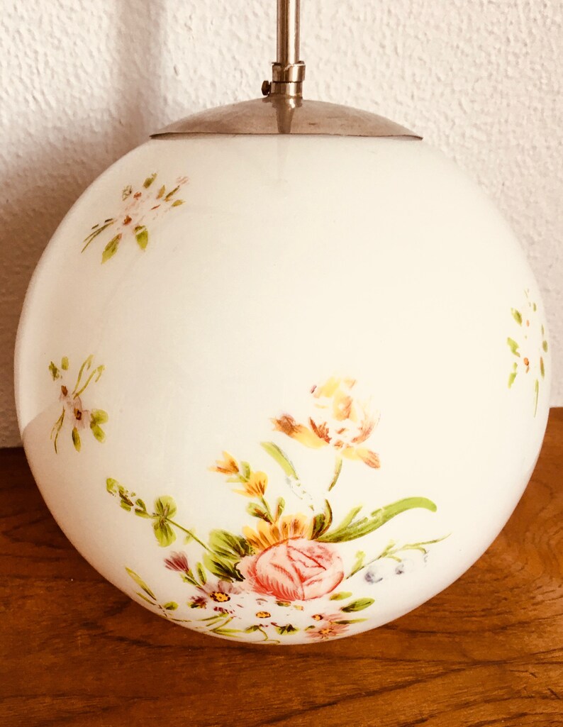 Peut inclure: Un luminaire suspendu en forme de globe en verre blanc avec un motif floral. Les fleurs sont peintes dans des tons de rose, jaune et vert.