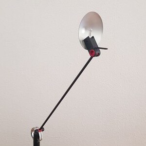 May include: A black desk lamp with a long, adjustable arm and a round, silver reflector. The lamp has a black base and a black shade.