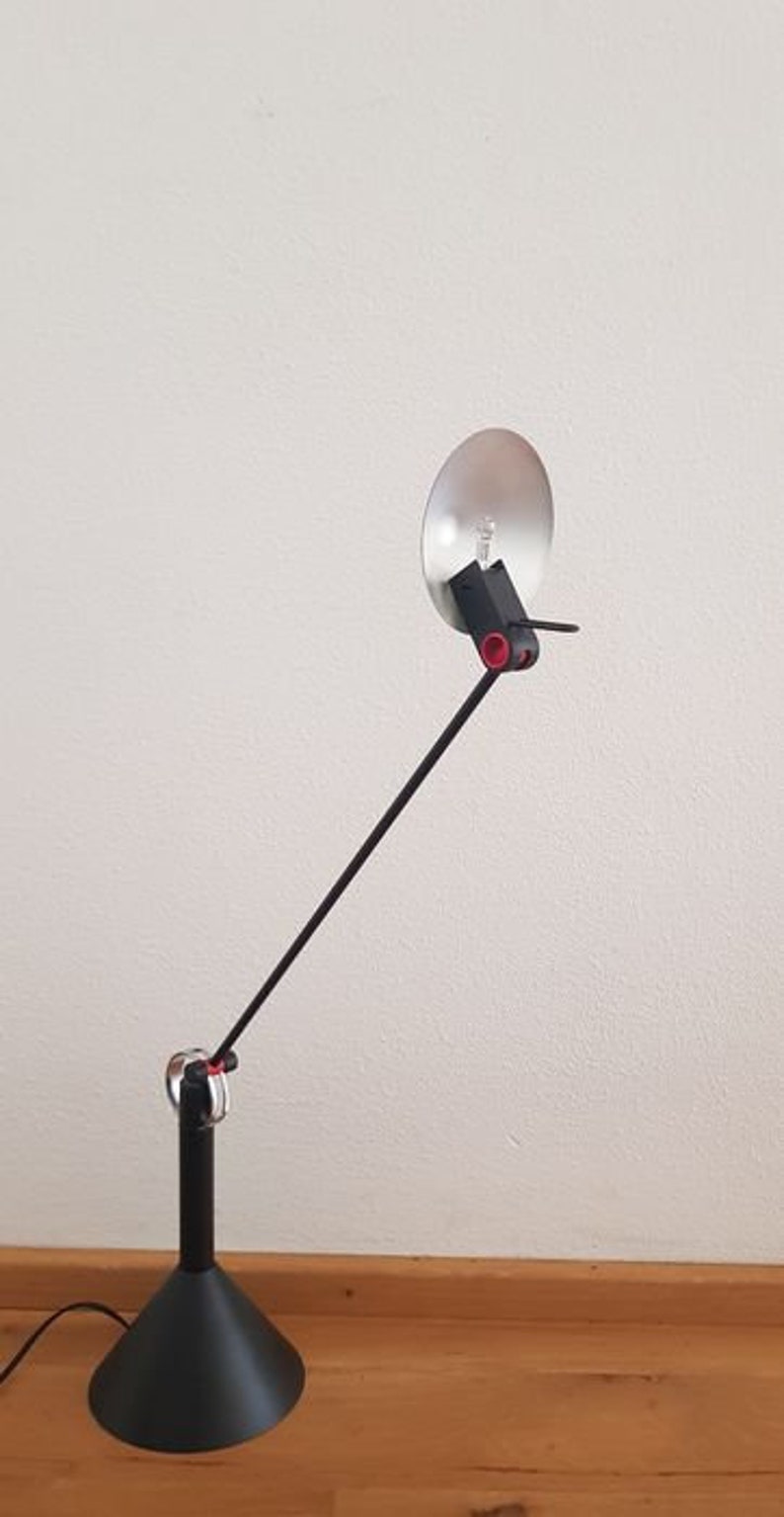May include: A black desk lamp with a long, adjustable arm and a round, silver reflector. The lamp has a black base and a black shade.