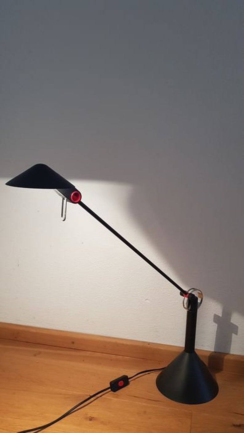 May include: A black desk lamp with a long, adjustable arm and a black shade. The lamp has a red switch and a black cord.