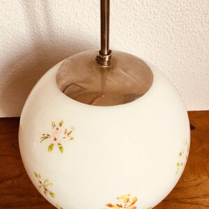 Peut inclure: Un luminaire suspendu en forme de globe blanc avec un dessus en m&eacute;tal argent&eacute; et des motifs floraux dans des tons de rose, jaune et vert.