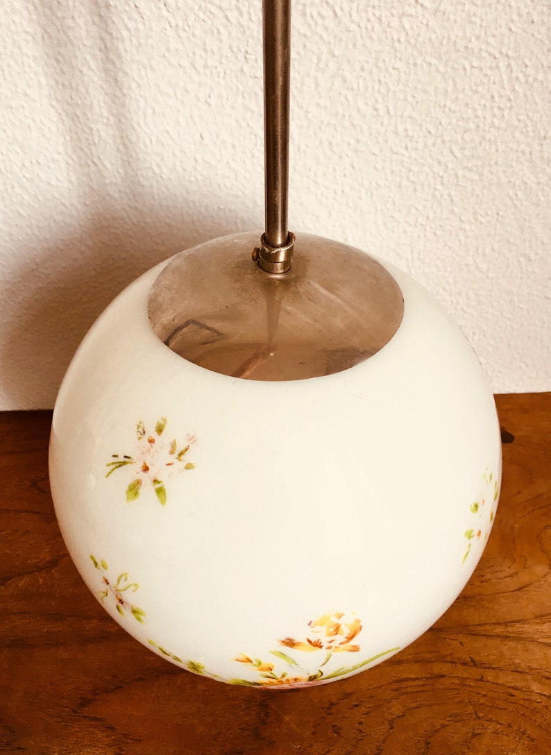 Peut inclure: Un luminaire suspendu en forme de globe blanc avec un dessus en m&eacute;tal argent&eacute; et des motifs floraux dans des tons de rose, jaune et vert.
