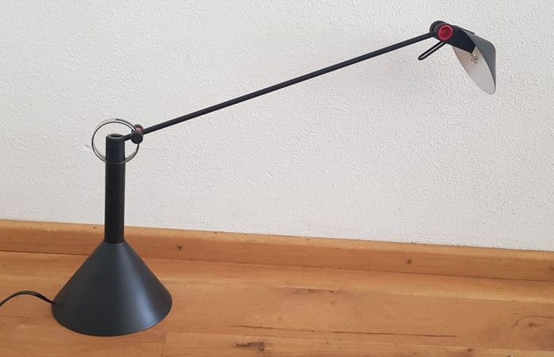 May include: A black desk lamp with a long, adjustable arm and a black, cone-shaped base. The lamp has a red knob on the arm and a white, circular light diffuser.