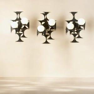Puede incluir: Tres apliques de pared de metal negro con diseños geométricos y bombillas blancas. Cada aplique tiene cuatro bombillas.