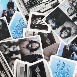 Peut inclure: Un collage d'autocollants présentant diverses images, notamment un groupe de musique, un écran d'ordinateur et une personne avec une corne de diable. Le texte "LOST MY TRAIN OF THOUGHT" est visible sur un autocollant bleu. Le texte "Tranquility Base Hotel + Casino" est visible sur un autocollant noir et blanc.