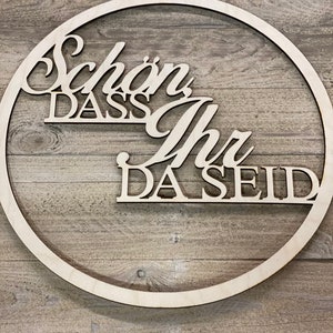 Könnte beinhalten: Ein Holz-Kreis mit den Worten "Schön dass ihr da seid" in einer dekorativen Schrift.