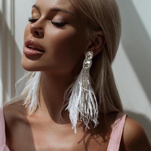 May include: A pair of long, white feather earrings with crystal accents. The earrings are dangling and have a silver chain.