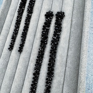 Könnte beinhalten: Vier Paar schwarze Perlenohrringe werden auf einer grauen Samtoberfläche präsentiert. Die Ohrringe sind lang und hängen, mit einer Ansammlung von Perlen oben und einem sich verjüngenden Design. Die Perlen haben eine facettierte, reflektierende Oberfläche.