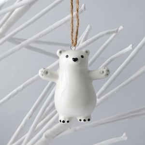 May include: White ceramic polar bear ornament with black eyes and nose, hanging from a brown twine string.
