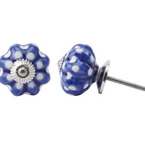 Puede incluir: Pomo de armario de cerámica azul y blanco con un centro plateado. El pomo tiene un borde festoneado y un patrón de lunares blancos.