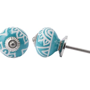Puede incluir: Dos pomos de armario de cerámica turquesa con diseños geométricos blancos. Un pomo está unido a un tornillo plateado.