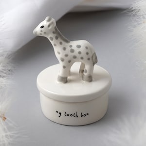 May include: A white ceramic tooth box with a grey and white giraffe figurine on top. The box has the words "my tooth box" written on the front.