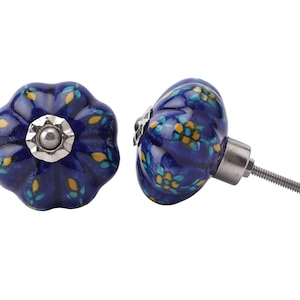 Pode incluir: Dois puxadores decorativos de cerâmica para armários. Os puxadores são azuis escuros com um padrão floral em amarelo e azul-petróleo. Cada puxador tem uma base e um parafuso de metal prateado para instalação.
