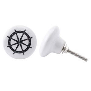 Pode incluir: Botão de armário de cerâmica branca com um design de roda de navio preto. O botão tem um parafuso prateado.