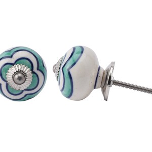 Könnte beinhalten: Weißer Keramik-Knopf mit einem grünen und blauen Blumenmuster. Der Knopf hat eine silberne Schraube und eine silberne Basis.