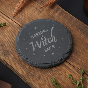 Puede incluir: Un posavasos redondo de pizarra negra con el texto "Resting Witch Face" grabado en letras plateadas.