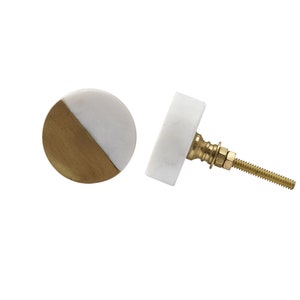 Może przedstawiać: Dwa okrągłe gałki do szafki z białym marmurowym wykończeniem. Jeden gałka ma złoty półkole na przodzie. Drugi gałka ma złotą śrubę i złotą nakrętkę.