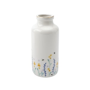 May include: White ceramic vase with a gold rim and a floral design featuring yellow, blue, and green flowers and bees.