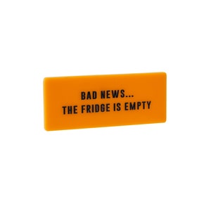 Op de afbeelding: Een oranje rechthoekig bord met de tekst "BAD NEWS... THE FRIDGE IS EMPTY" in zwart.