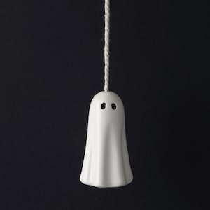 May include: A white ceramic ghost with two black eyes hanging from a white string. The ghost is a light pull for a lamp.