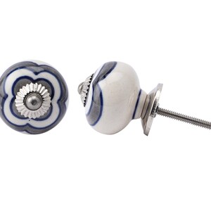 May include: Two ceramic cabinet knobs. One is round with a floral design in white, grey, and navy blue. The other is oval with a navy blue and grey design. Both have silver metal hardware.