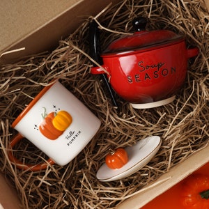 May include: A gift set featuring a white ceramic mug with a pumpkin design and the text "Hello Pumpkin" and a red ceramic soup bowl with the text "Soup Season".