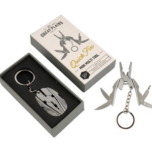 Puede incluir: Un llavero multiherramienta plateado con su caja. La caja es blanca con el texto "Quick Fix - Mini Multi Tool" y un gráfico de la herramienta. El llavero está en una caja gris con interior negro. La multiherramienta tiene alicates y otras herramientas.