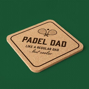Puede incluir: Posavasos cuadrado de corcho con esquinas redondeadas. El posavasos presenta el texto "PADEL DAD" sobre la frase "LIKE A REGULAR DAD...but cooler" en negro. Encima del texto hay dos raquetas de pádel cruzadas y una pelota.