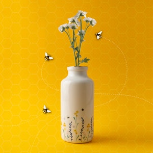 Può includere: Un vaso di ceramica bianco con un motivo floreale e un mazzo di fiori bianchi. Quattro api volano intorno al vaso su uno sfondo giallo a nido d'ape.