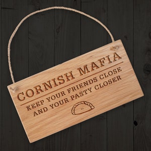May include: A wooden sign with a rope hanger reads "Cornish Mafia Keep your friends close and your pasty closer". A pastry is illustrated below the text.