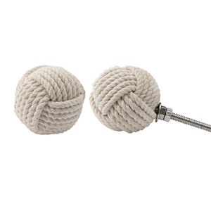 May include: Two off-white rope knot cabinet knobs. One knob is attached to a metal screw and hardware. The knobs are round and made of tightly wound rope, creating a nautical or coastal theme.
