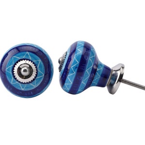 Peut inclure: Deux boutons de meuble décoratifs. Les boutons sont ronds avec un motif géométrique bleu et blanc. La quincaillerie est de couleur argentée. Un bouton est montré de côté, révélant la vis. L'autre bouton est montré de face.